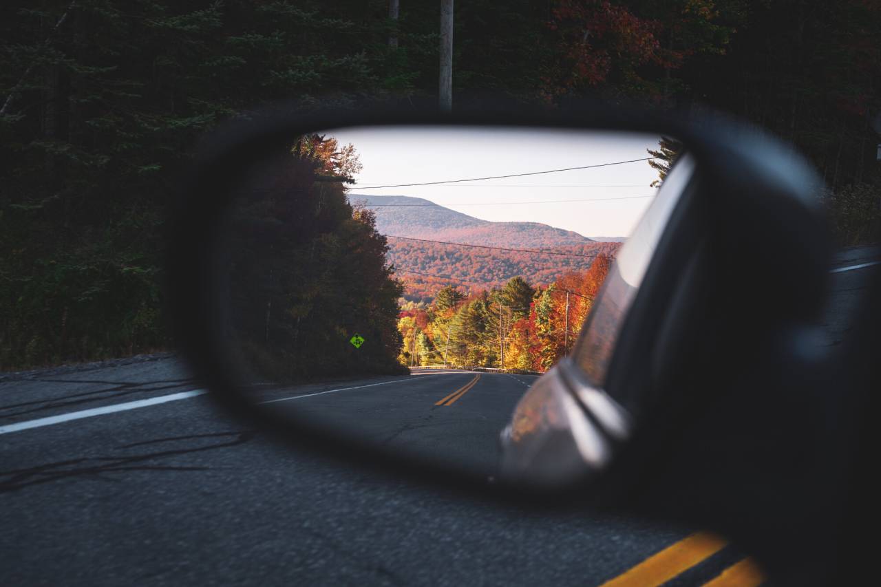 A fall landscape caught in the rearview mirror of a car.