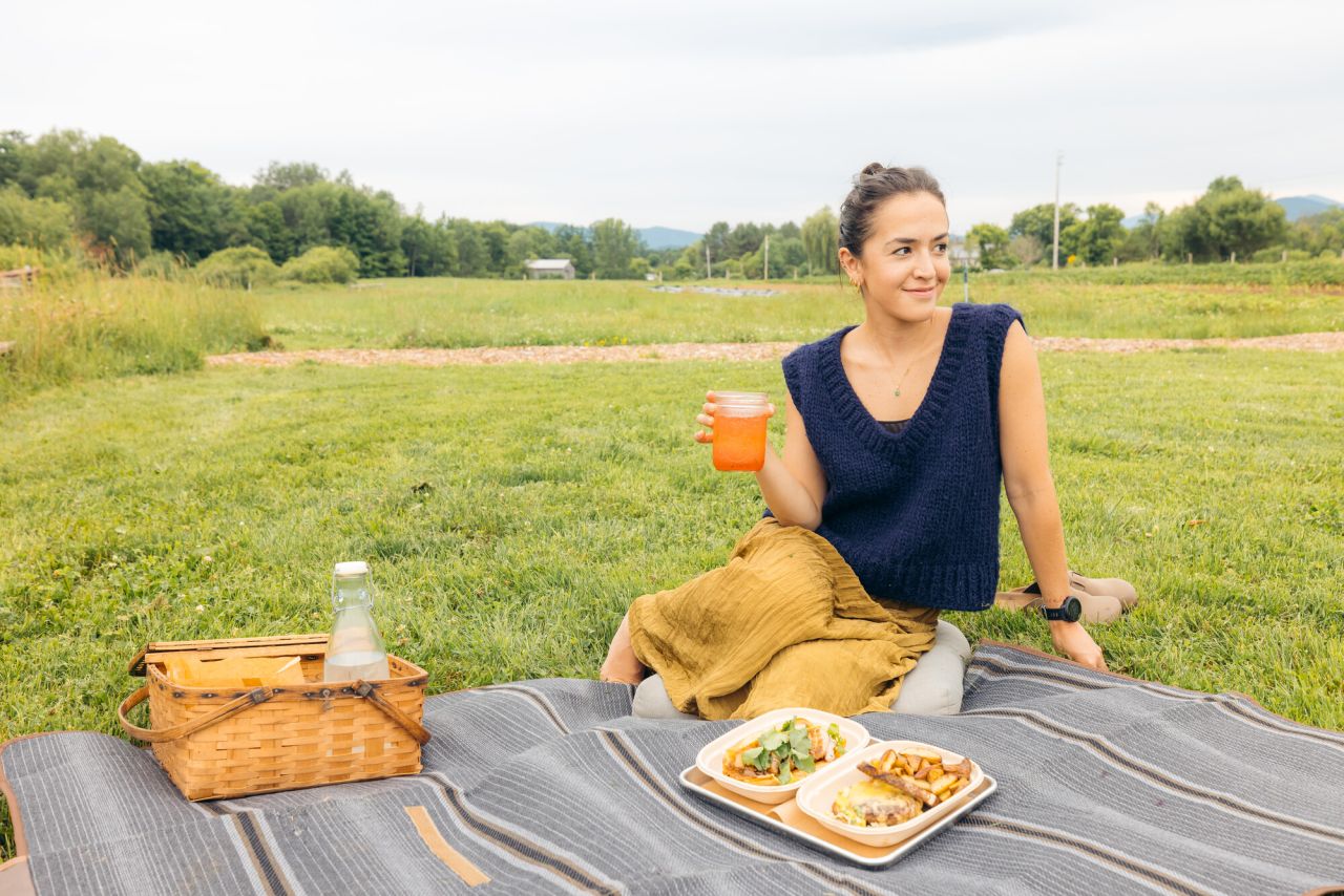 A woman has a picnic in a country field.
