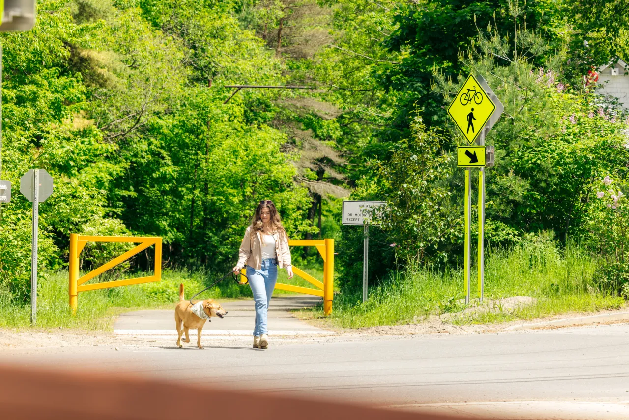 A woman walks her dog on a paved trail in spring. 