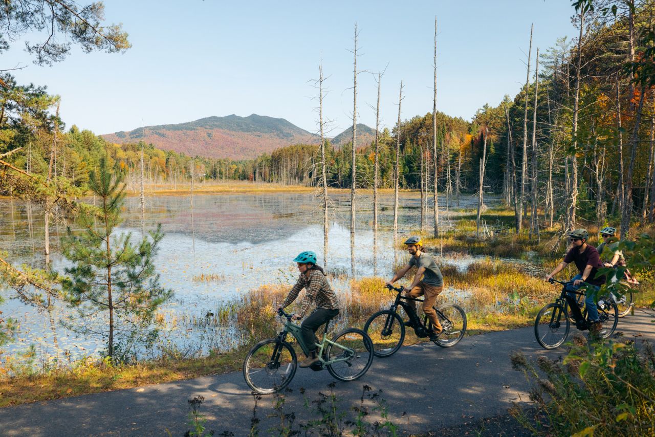 A group of cyclists ride along a lake. 