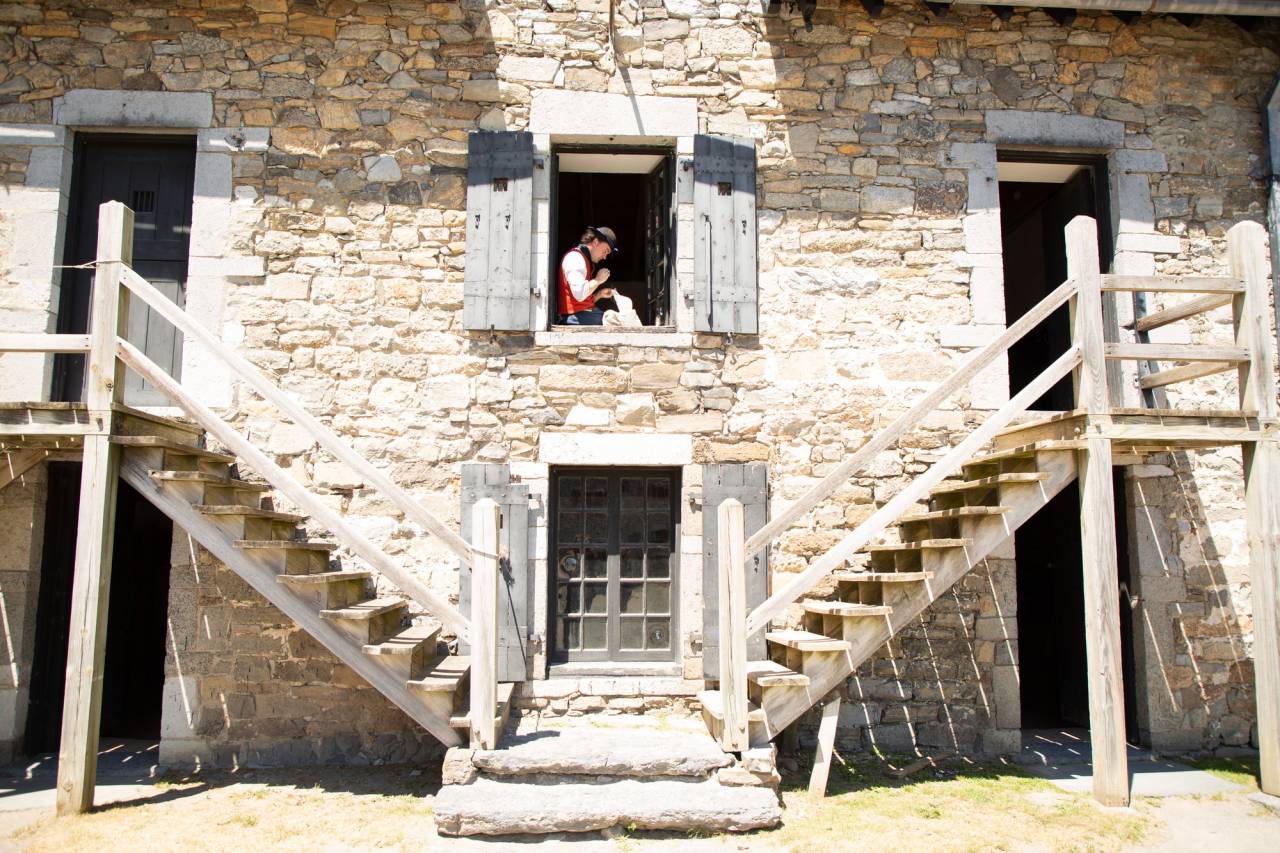 A man in colonial clothes sits in a historic fort window. 