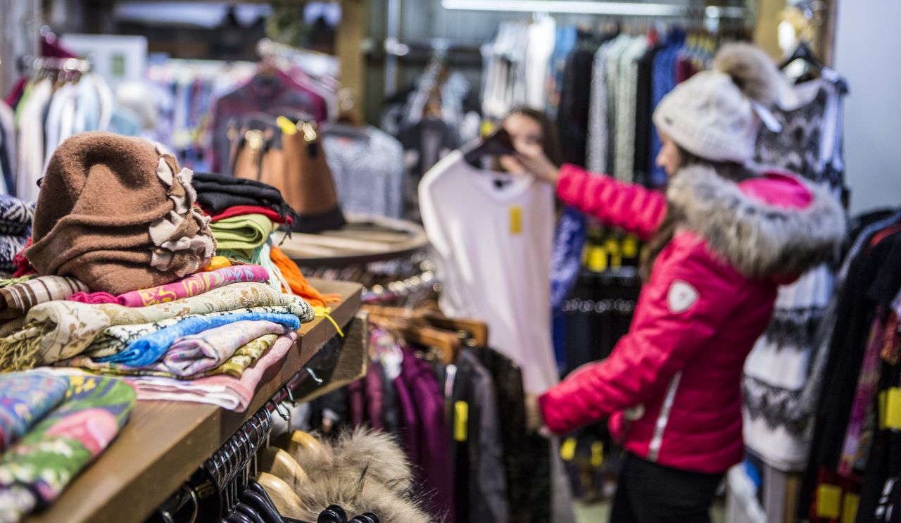 A woman in a red coat shops for clothing in a country store. 
