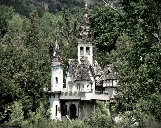 The exterior of a decaying children's castle amid an overgrown forest.
