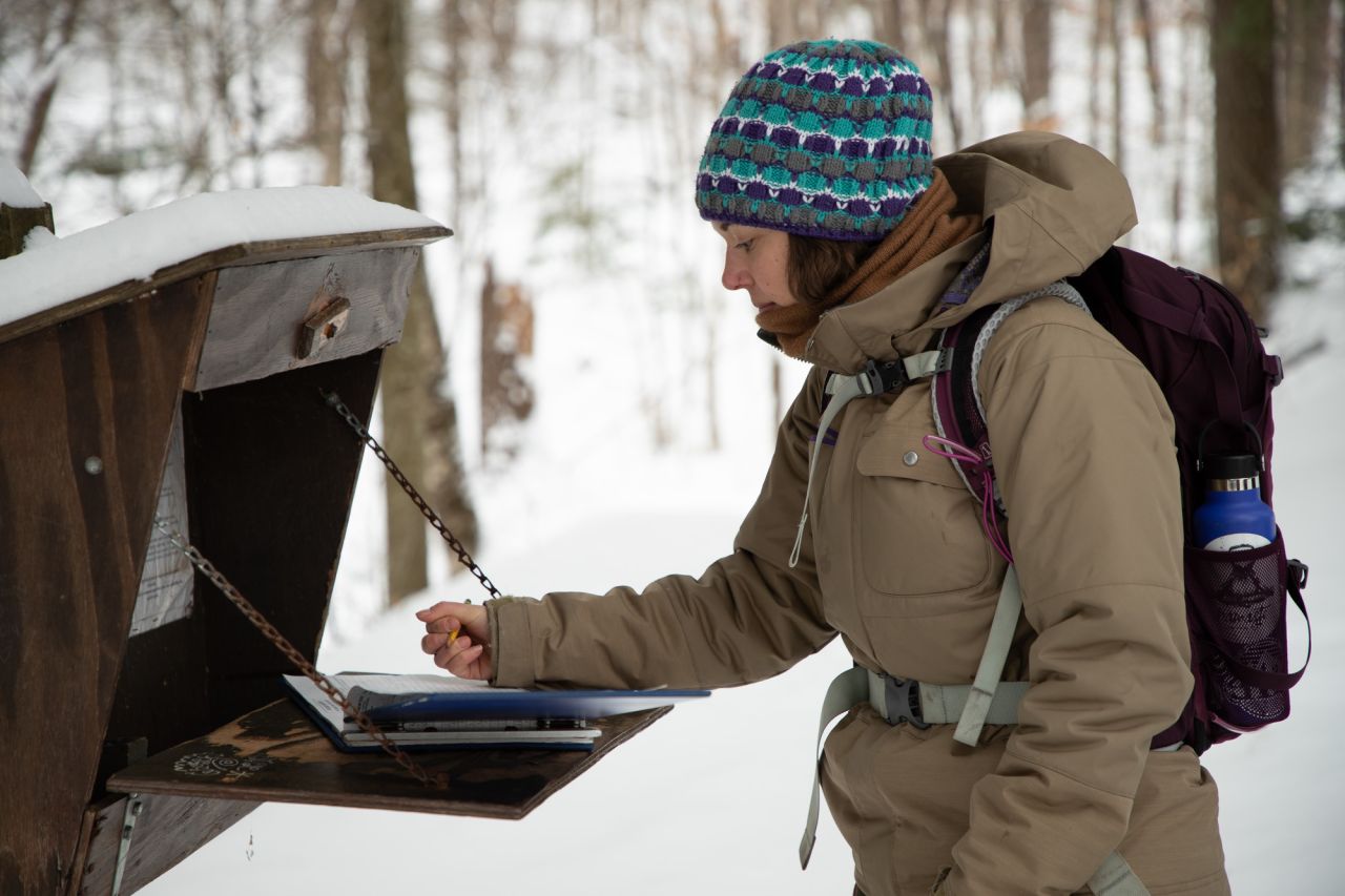 A woman signing into a trail register in winter.