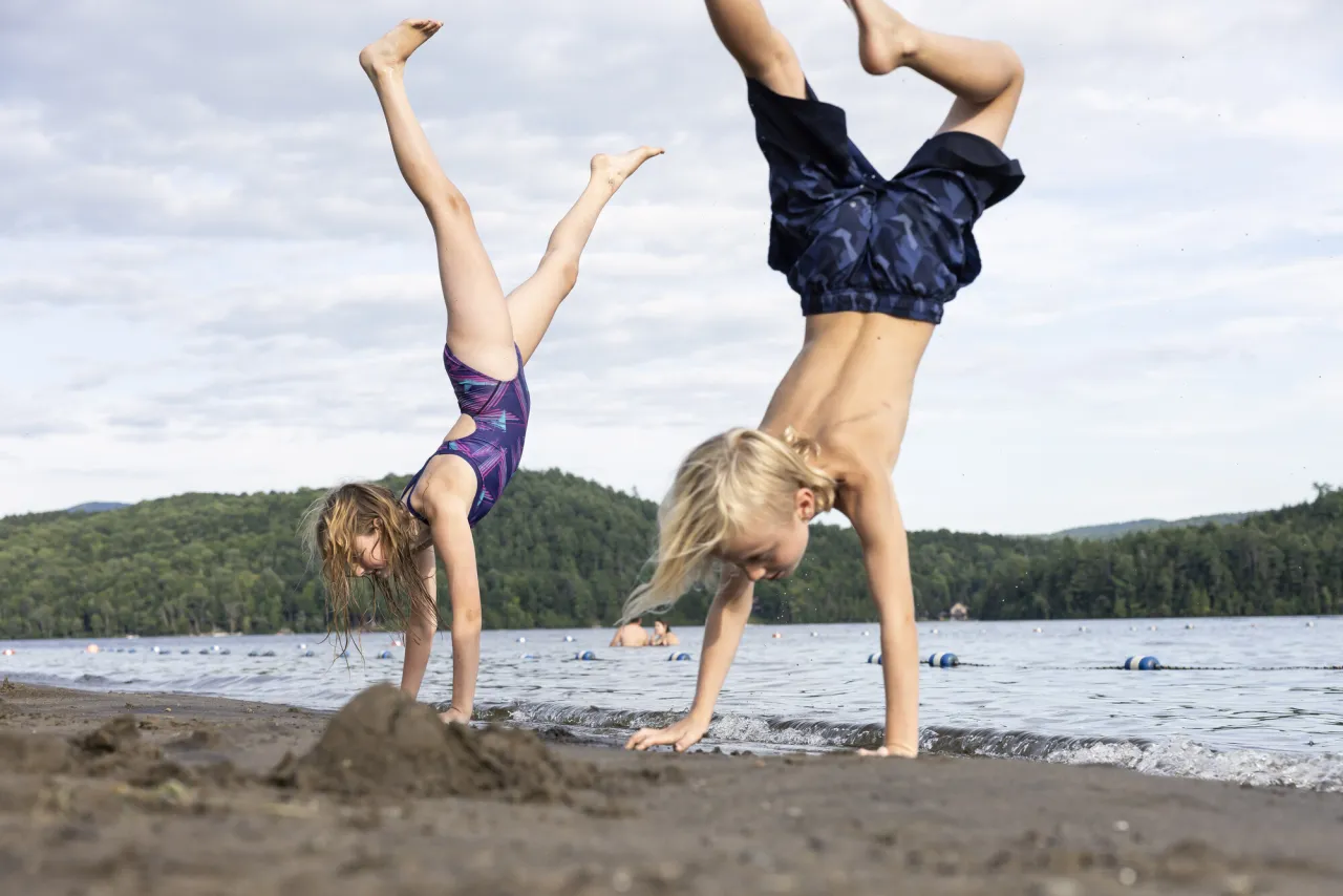 Two kids do cartwheels on a beach.