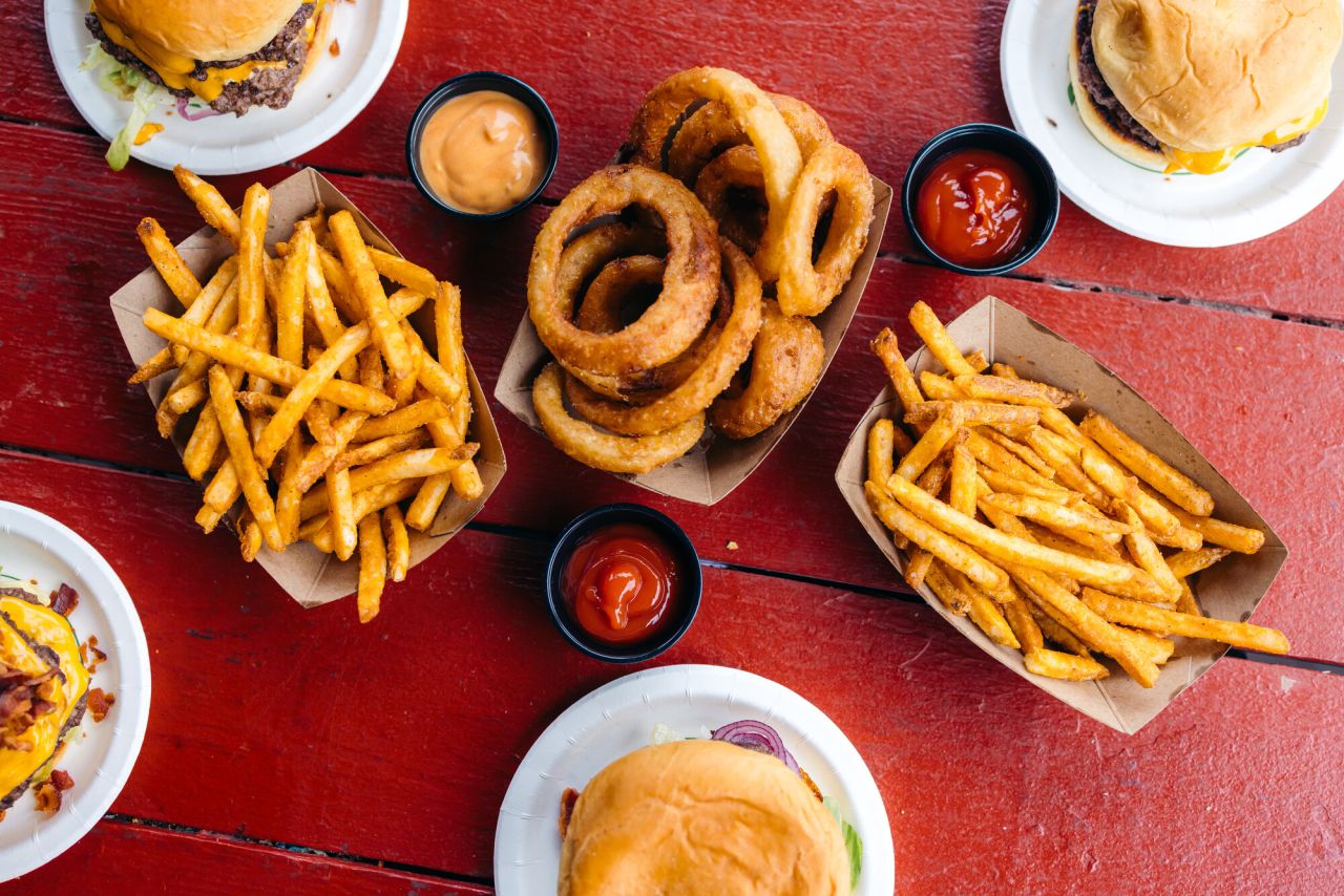A red table filled with burgers, onion rings, and french fries. 