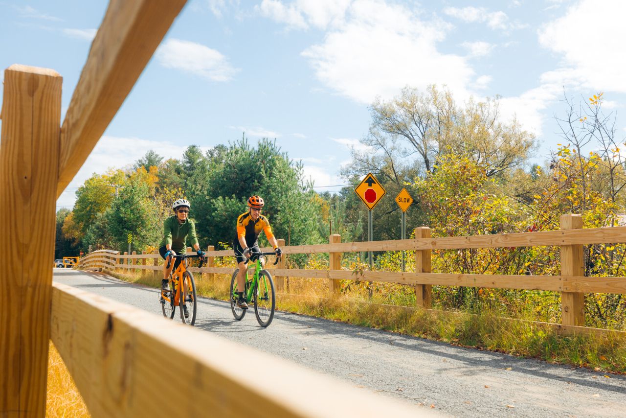 Two cyclists ride on a fenced in trail.
