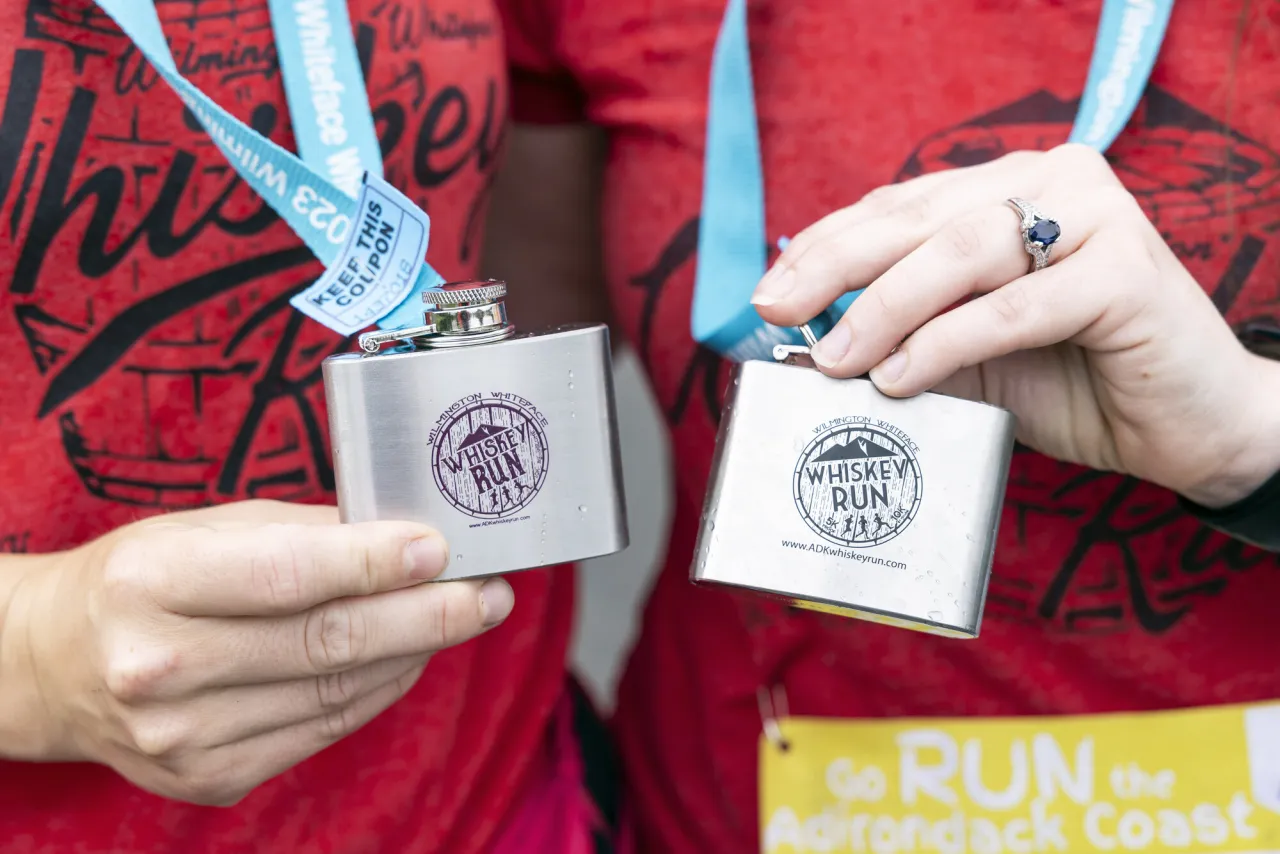 Two people hold up tiny flasks as medals for a 10k race.