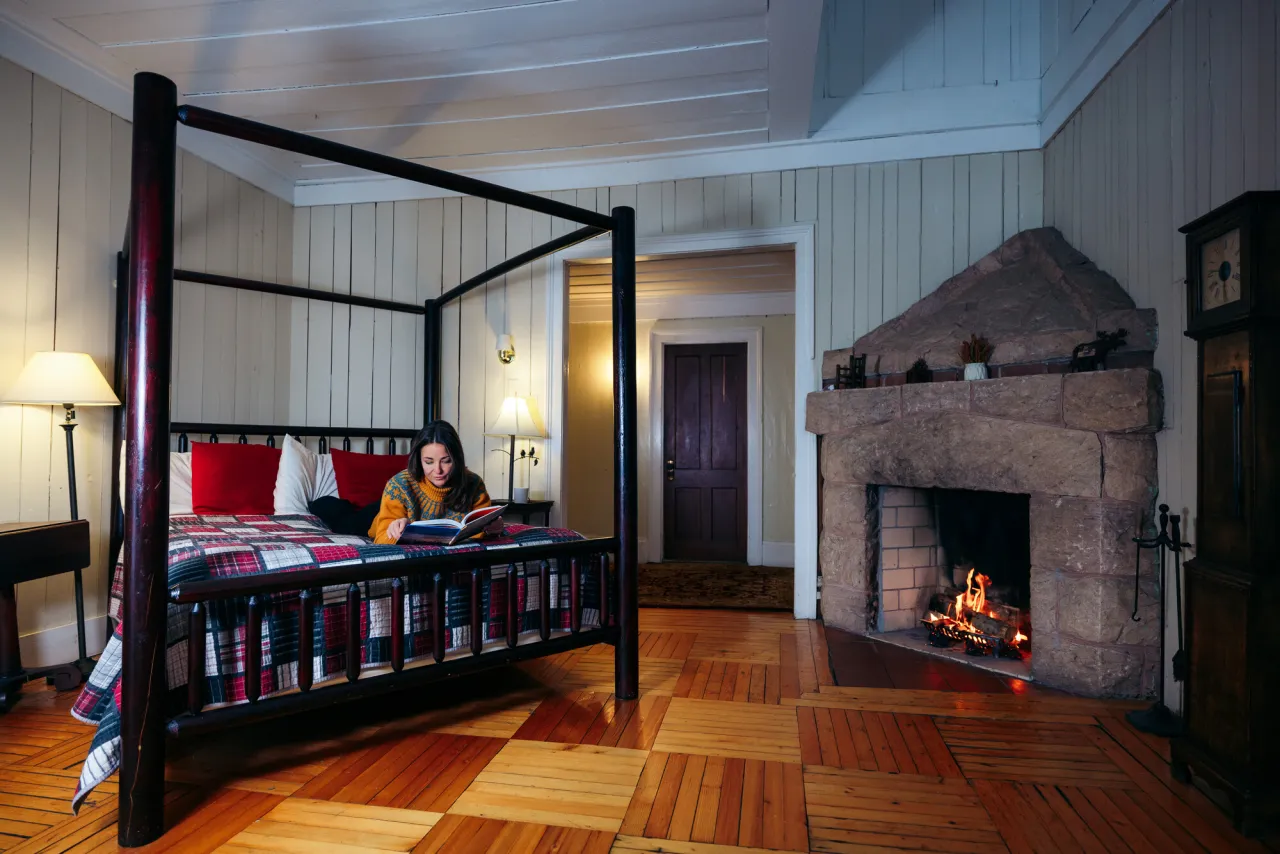A woman reads a book on a bed in a cabin.
