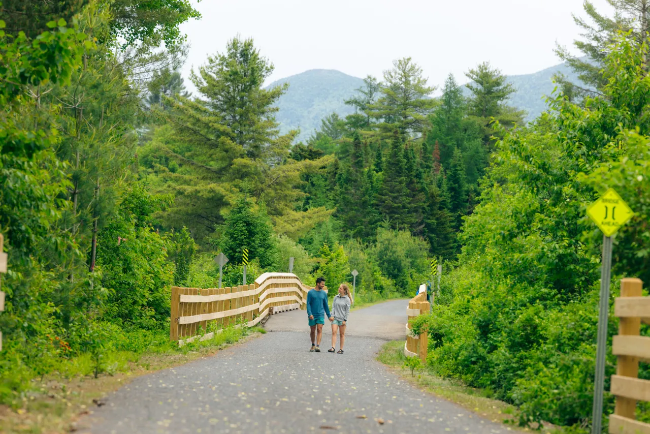A man and woman walk a paved trail in summer. 