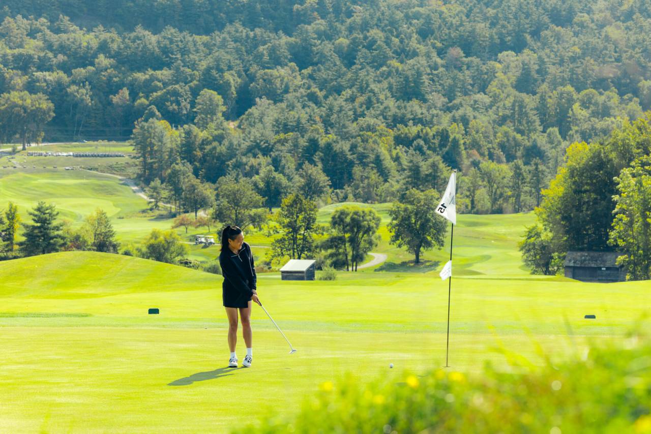 A woman puts a golf ball into a hole on a golf course. 