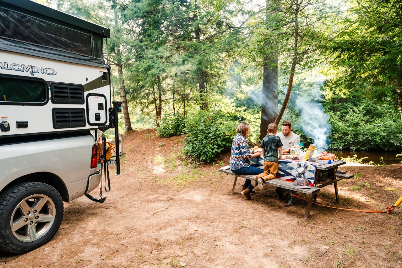 A man and woman eat lunch with their young son at a picnic table at their campsite. 