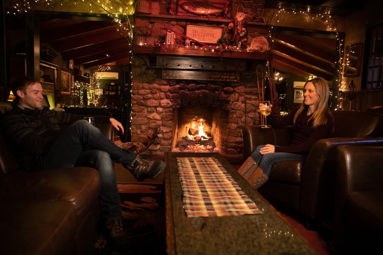 A man and woman share drinks at a stone fireplace.