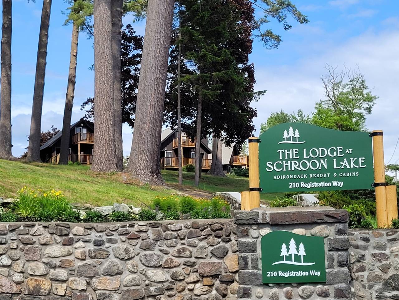 The front of a resort with sign and stone wall. 