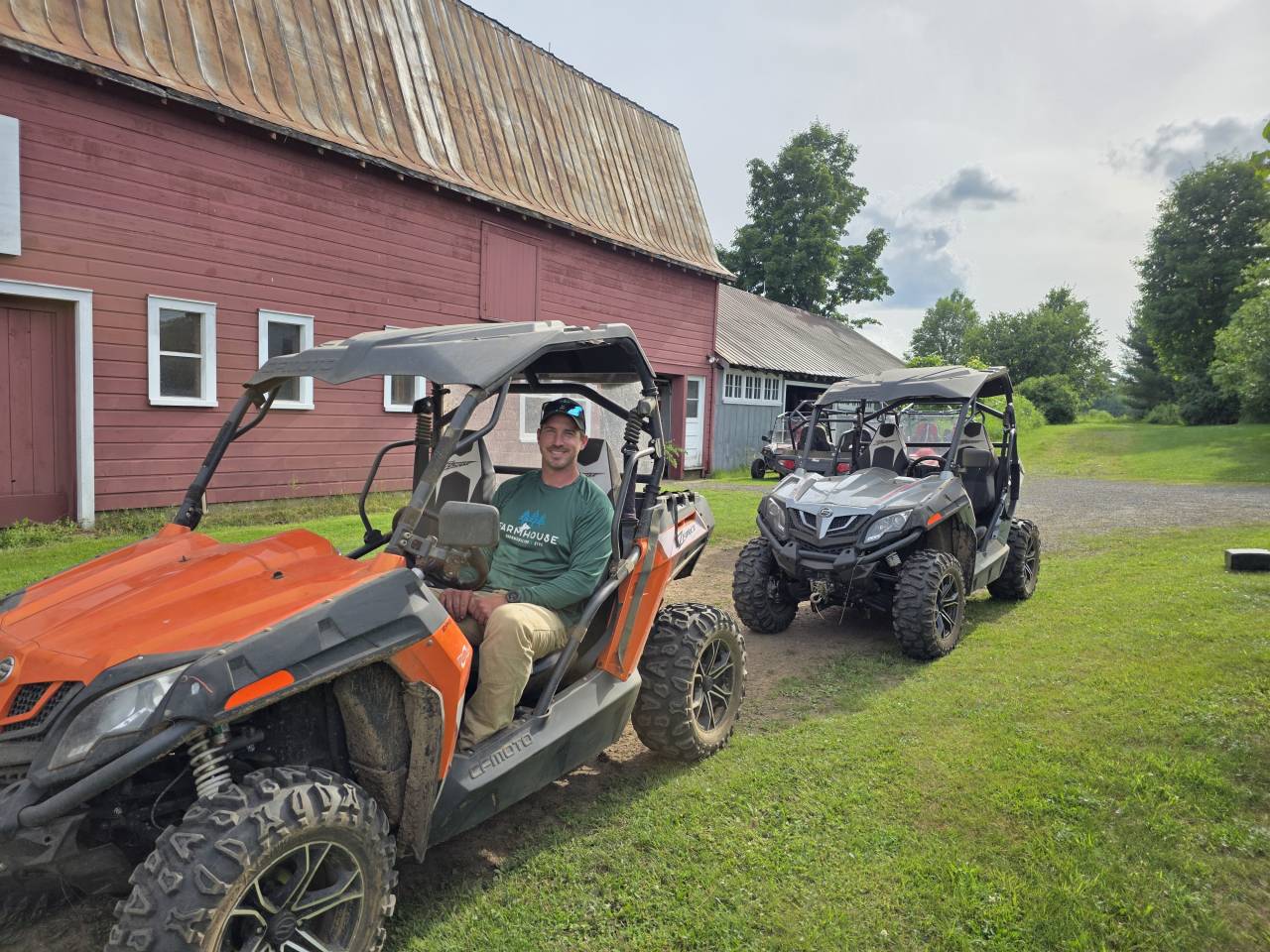 Man sitting in an orange UTV in front of Red Barn.