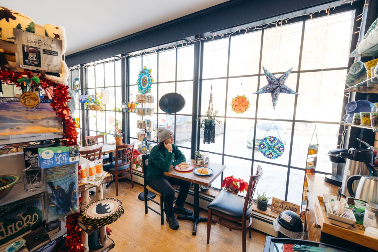 A man in winter gear looks out the window of an eclectic store.