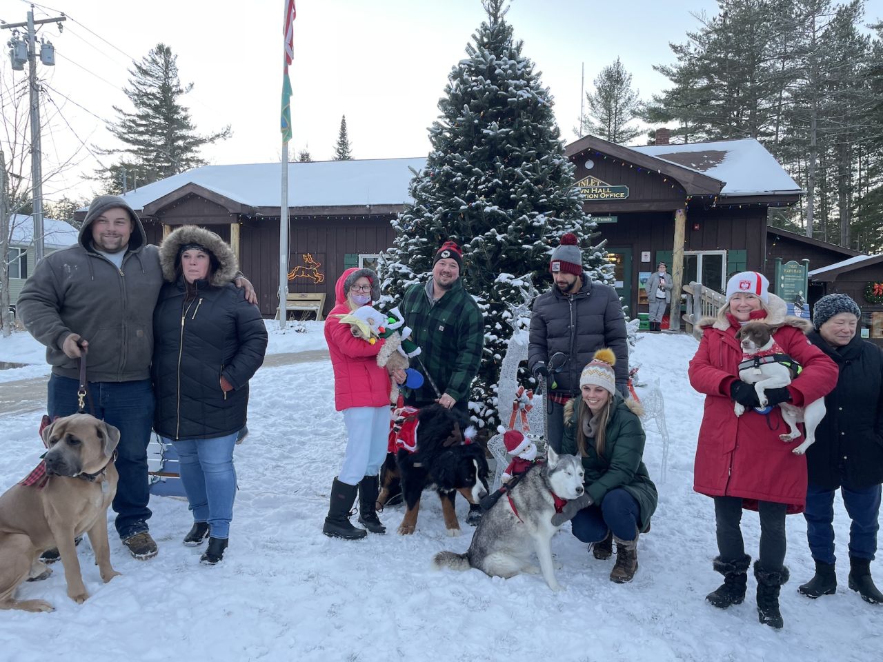 A group of people in winter gear and a dog pose for a picture in the snow in front of a large evergreen tree. 