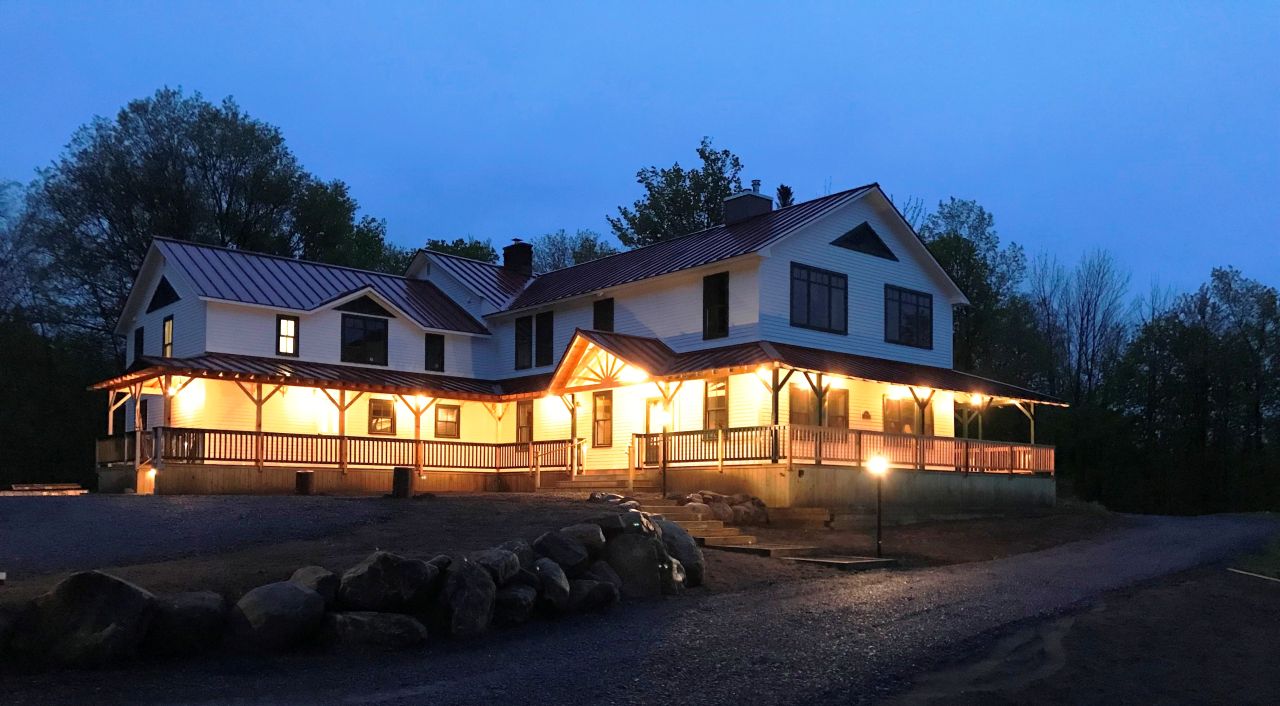 An inn with a lit up wrap around porch at night.