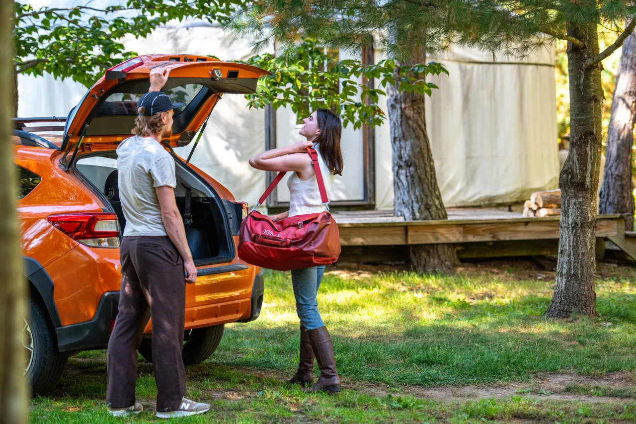 A man and woman unload an orange car at a cabin stay.