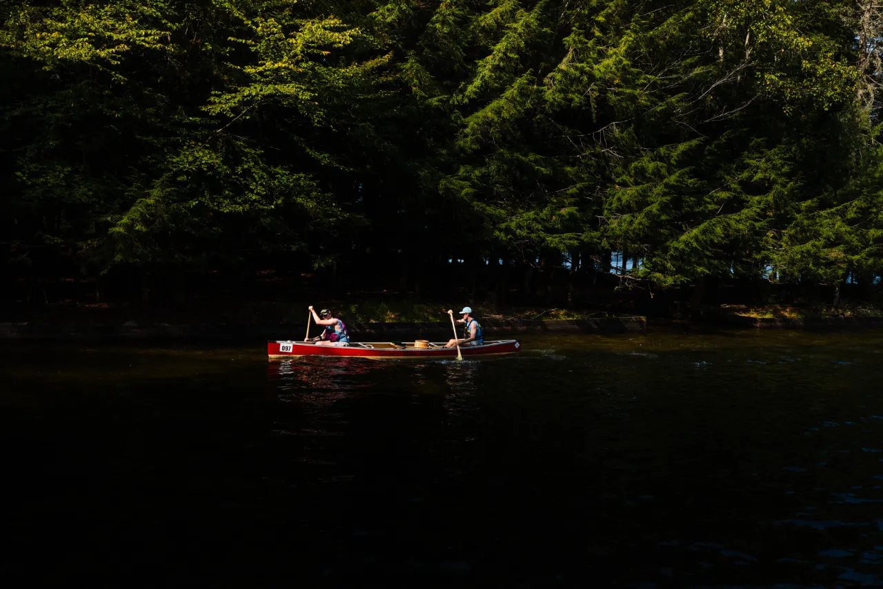 Two people paddle in  a canoe on a river in summer.