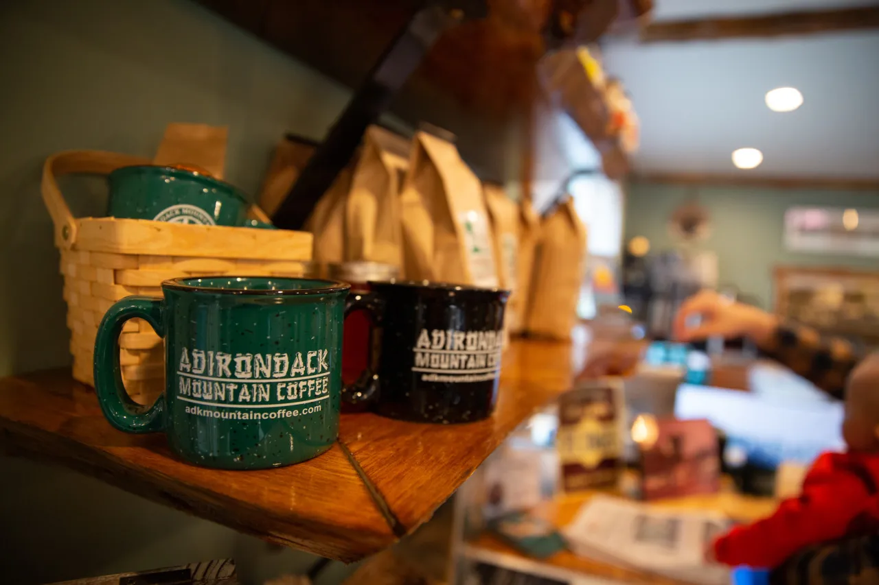 Adirondack Mountain Coffee Cafe mugs and bags of coffee sit on wooden shelf in cafe
