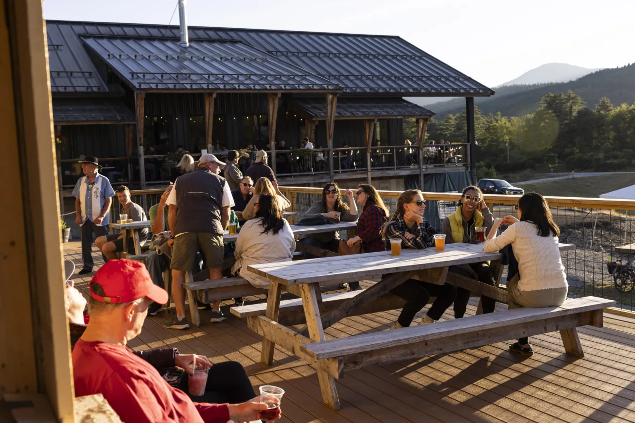 A group of people sit at picnic tables at a brewery outside.