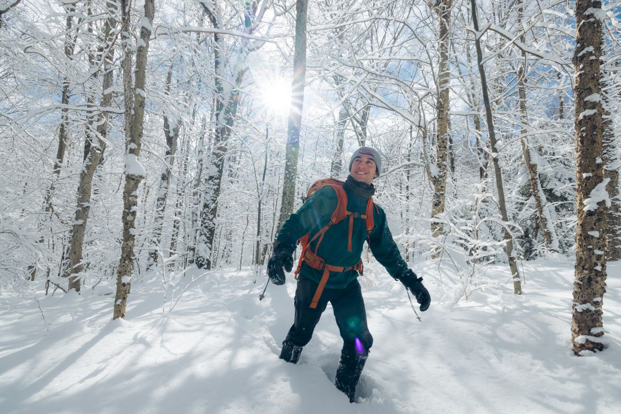 A man climbs through a bright snowy forest in snowshoes.