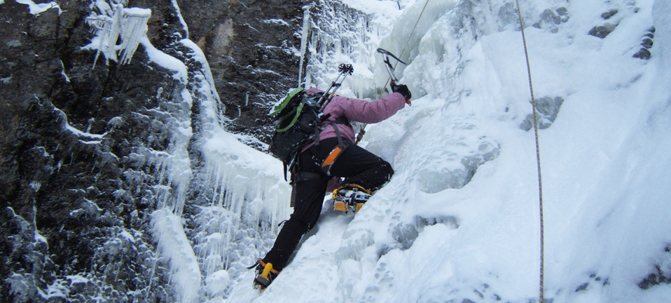 A man uses a pick while climbing up ice in winter.