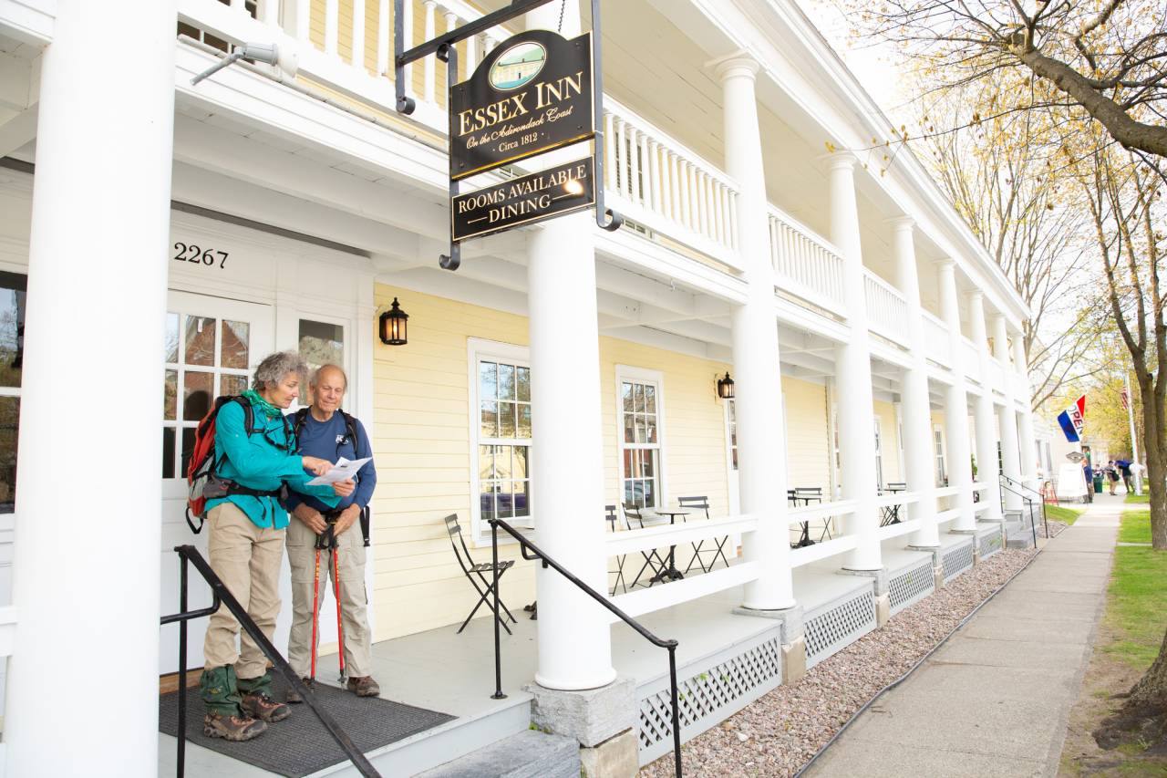 Two people stand on the porch of a white inn. 