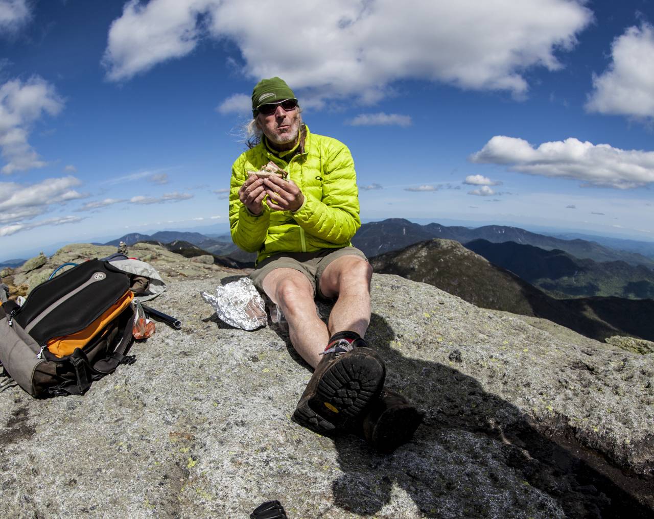 A person eating a sandwich on a mountain summit.