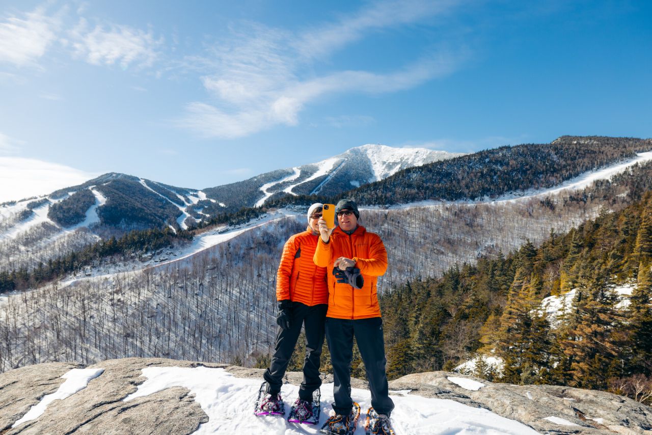 A couple snowshoeing at taking a selfie in front of Whiteface Mountain.