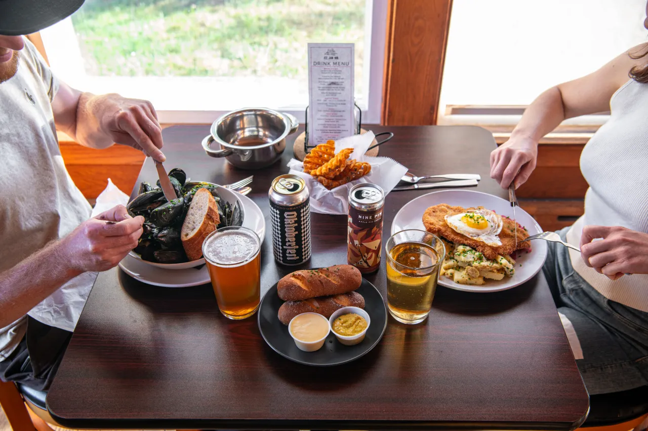 A man and woman eat dinner next to a window at a restaurant with beer.
