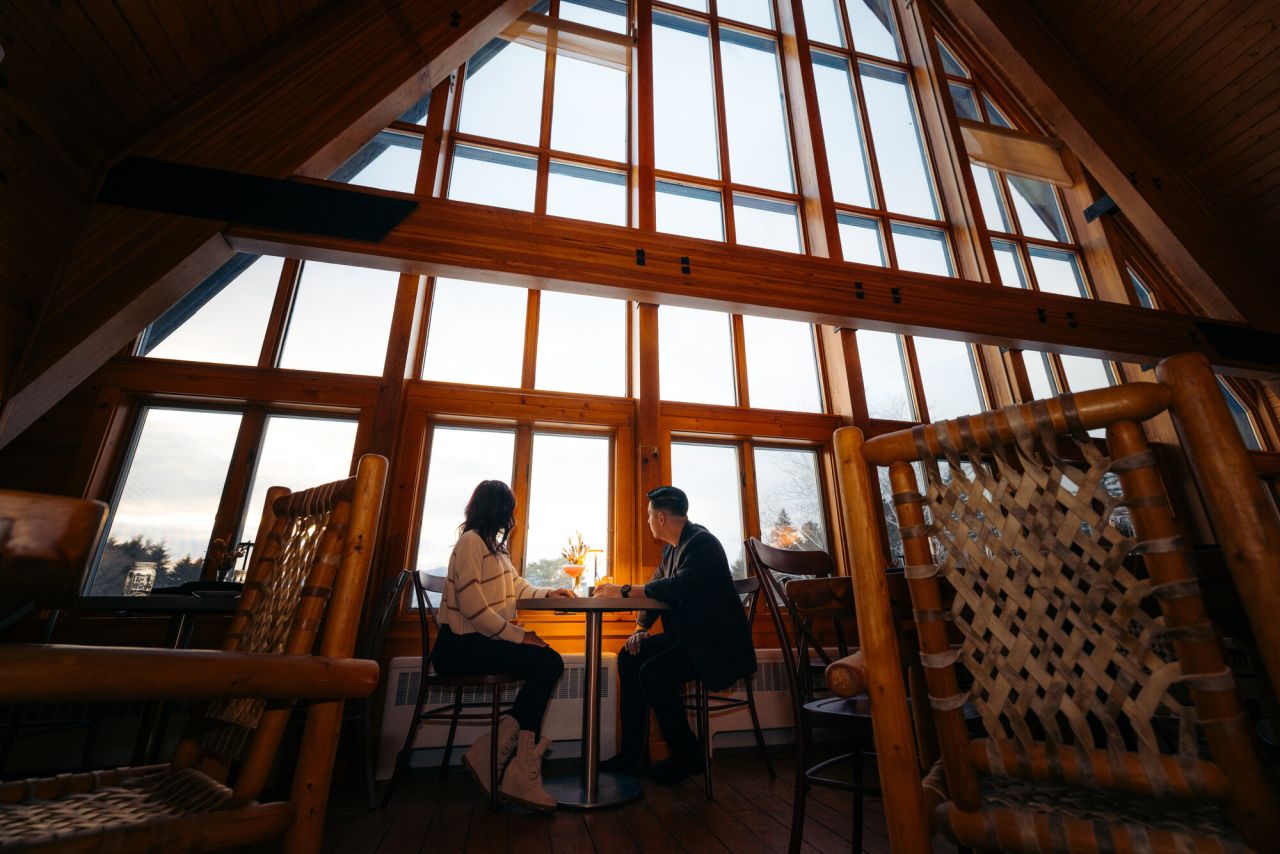 A man and woman dine in a grand A-frame restaurant with floor to ceiling windows. 