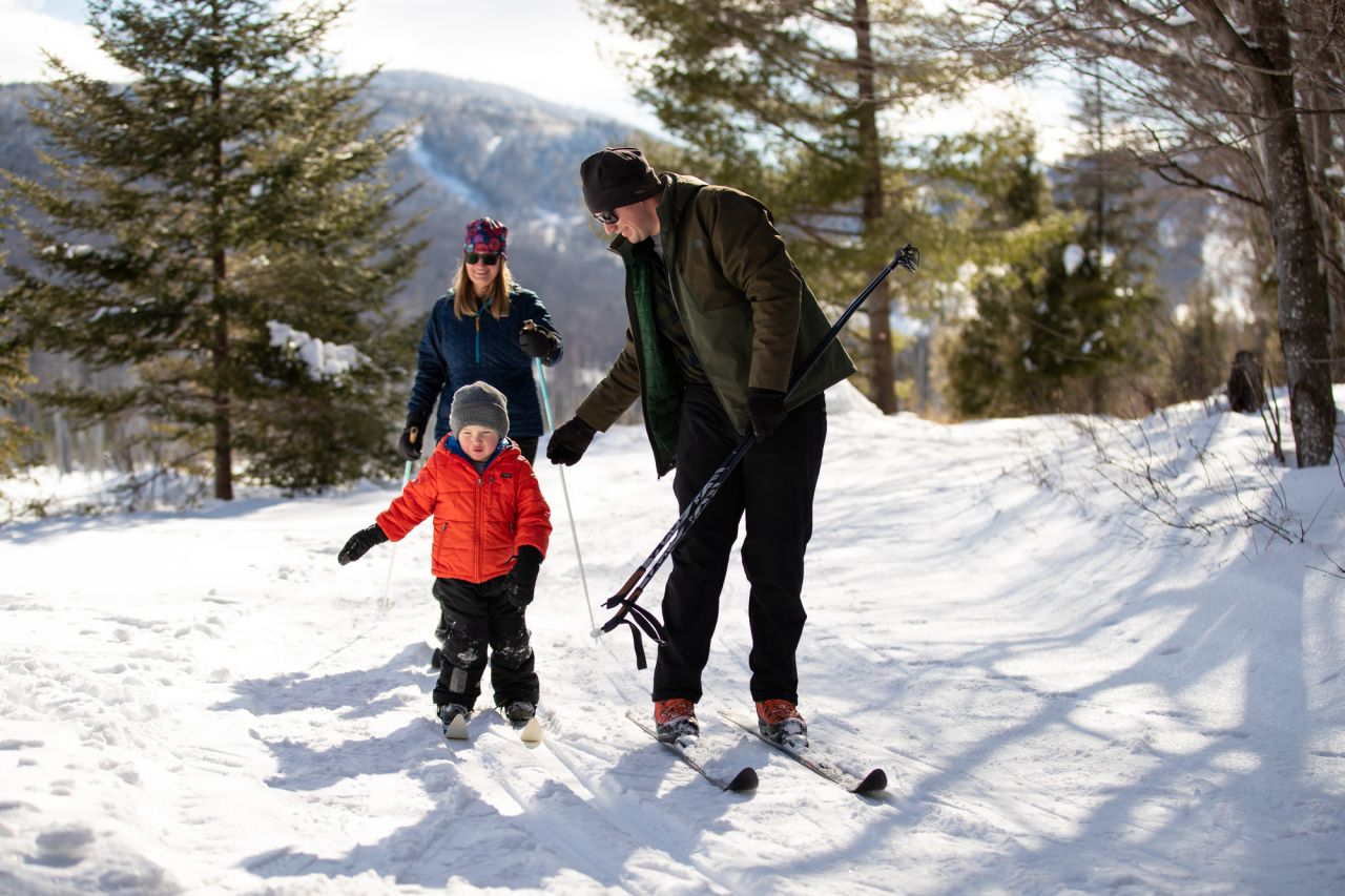 A man and woman cross-country ski with their young son on a sunny day. 