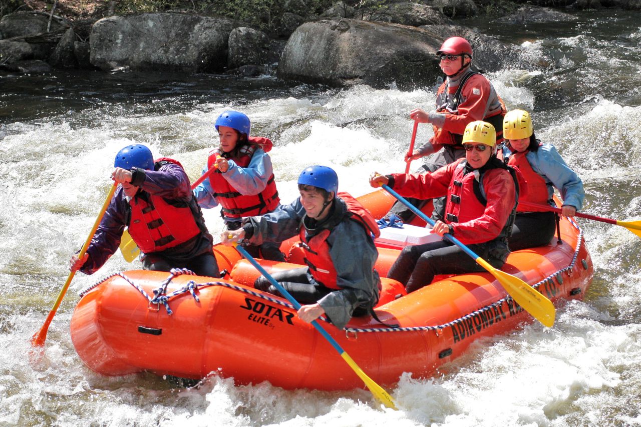 A group of adults in life jackets and helmets on a raft on a raging river.