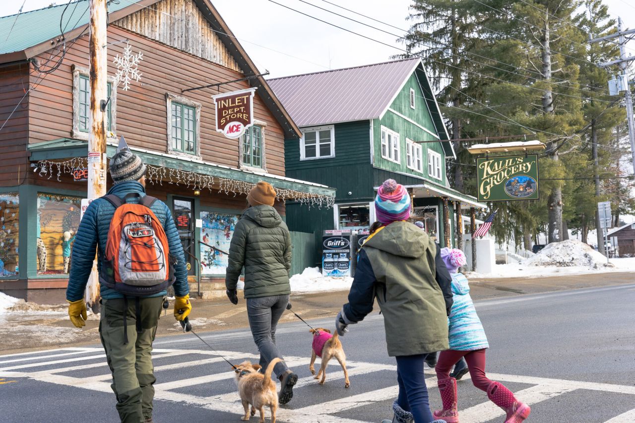 A family of four with two small dogs runs across the street to two country stores. 