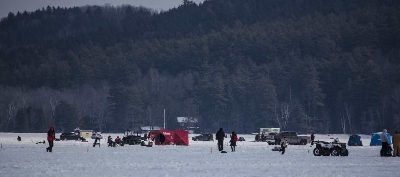 People ice fishing on Schroon Lake amongst tents, shanties, and vehicles