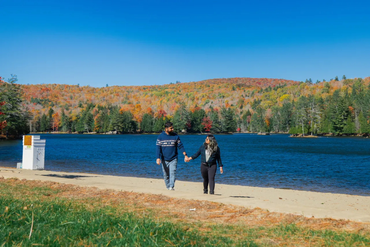 A man and woman walk on a lake beach in fall.