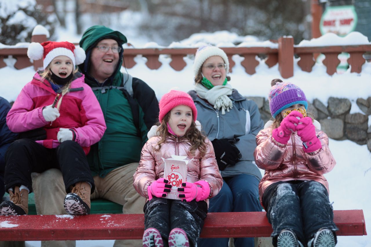 A man and woman and their three young daughters watch a performance at an outdoor winter event.