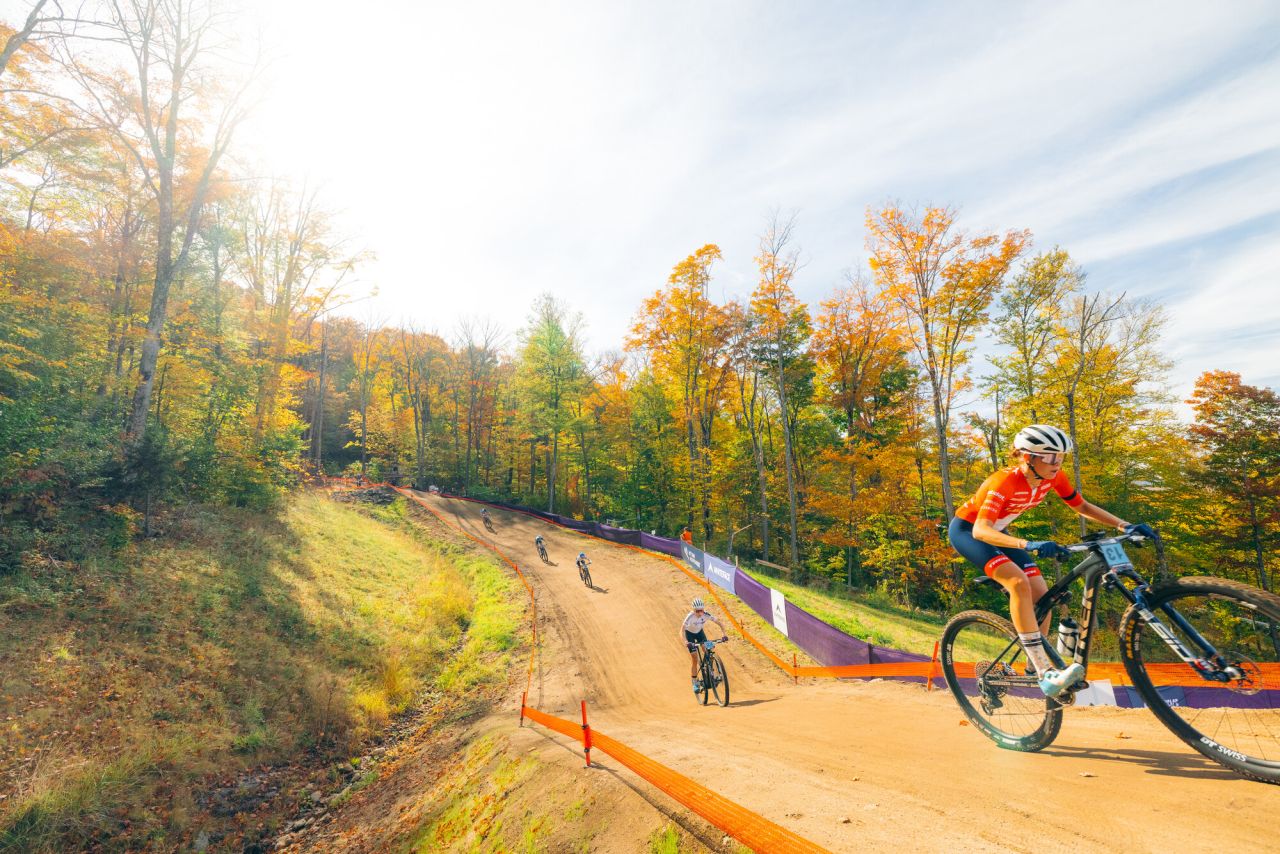 A pack of cyclists ride on a dirt track. 