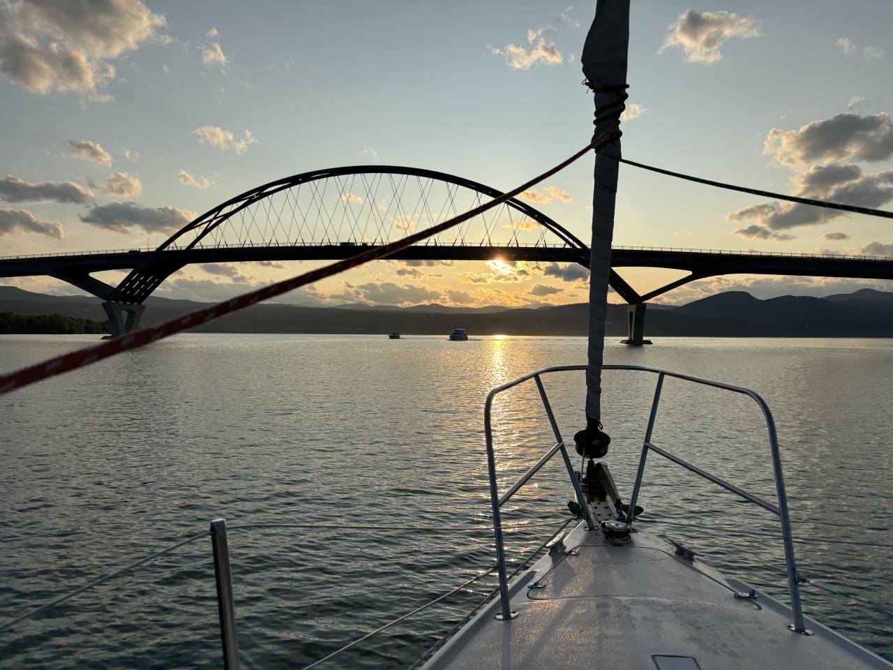 A sailboat on Lake Champlain with a view of the Champlain Bridge.