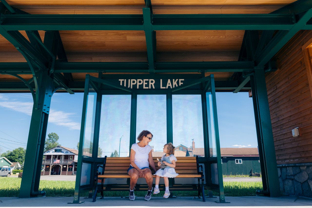 A woman and her daughter sit at an open train stop in Tupper Lake.