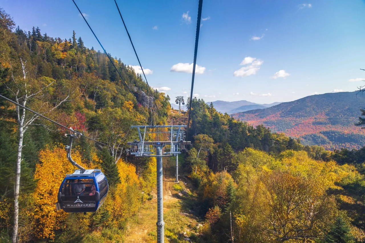 A gondola carries people over a mountain range in fall.