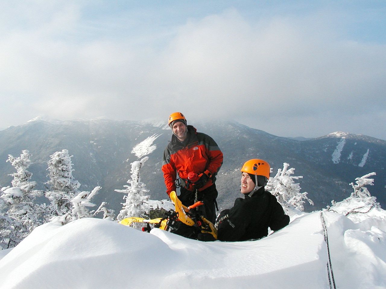 Two men smile and pose on top of a snowy mountain.
