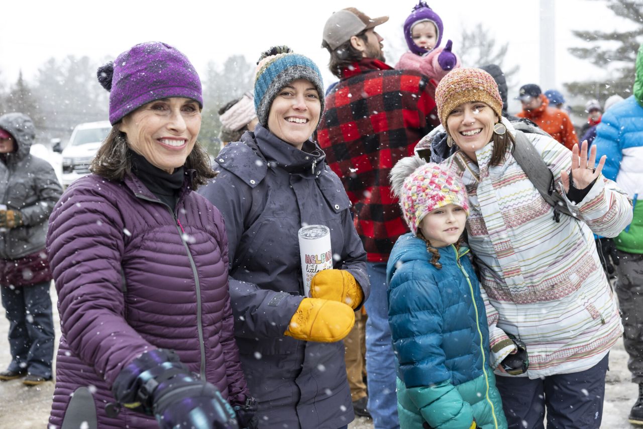 A group of women and children bundled in winter clothes smile and laugh at an event. 