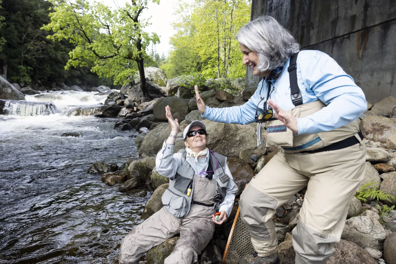 Two women high five in a stream while fly fishing. 