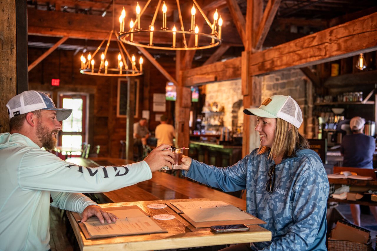 A man and woman cheers drinks in a warm lit rustic restaurant.