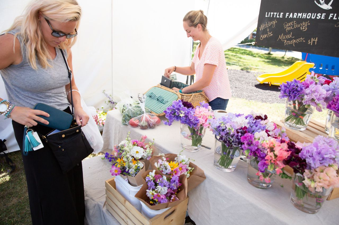 A woman opens her purse to pay for flowers at a farm stand. 