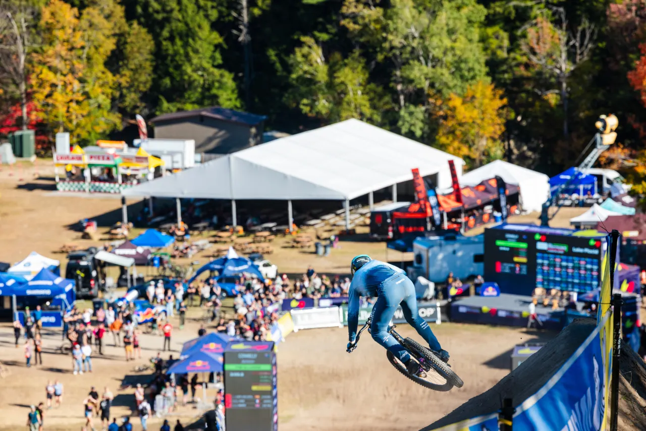 A mountain biker rides down a hill to a crowd cheering below.