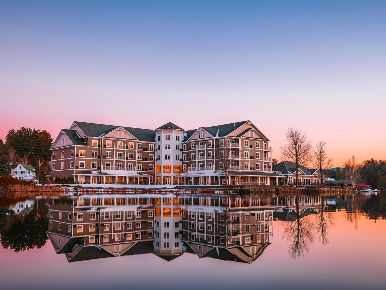 A sprawling hotel sits on the edge of a lake in early winter with the sun rising in the background.